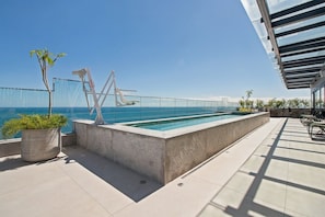 Ein Pool auf dem Dach mit freiem Blick auf das Meer, einer Glasbrüstung und Sitzgelegenheiten im Freien.
