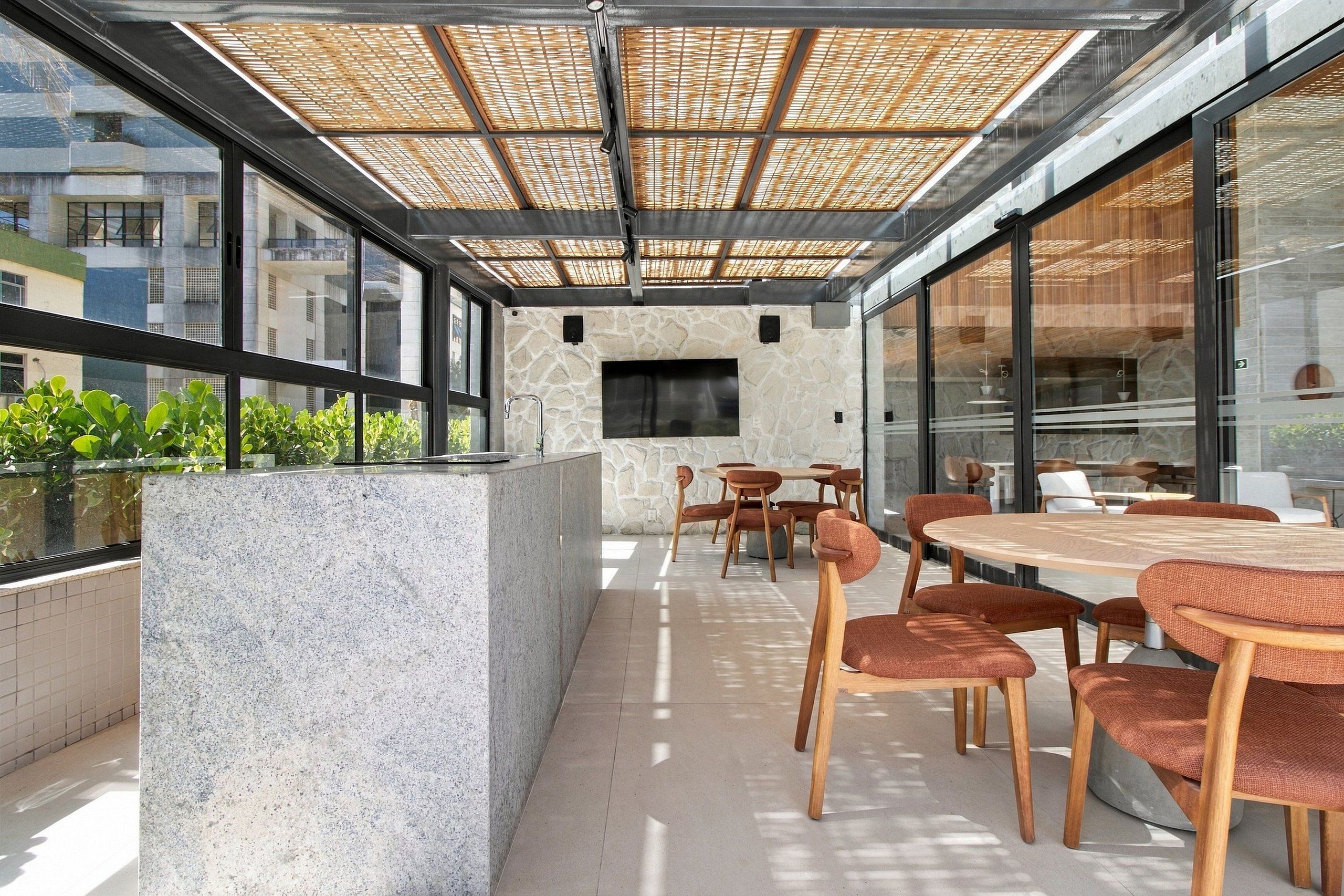An outdoor patio with a stone wall, a flat-screen TV, and a seating area with wooden tables and chairs.