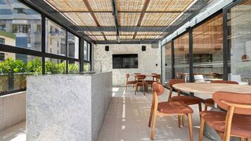 An outdoor patio with a stone wall, a flat-screen TV, and a seating area with wooden tables and chairs.