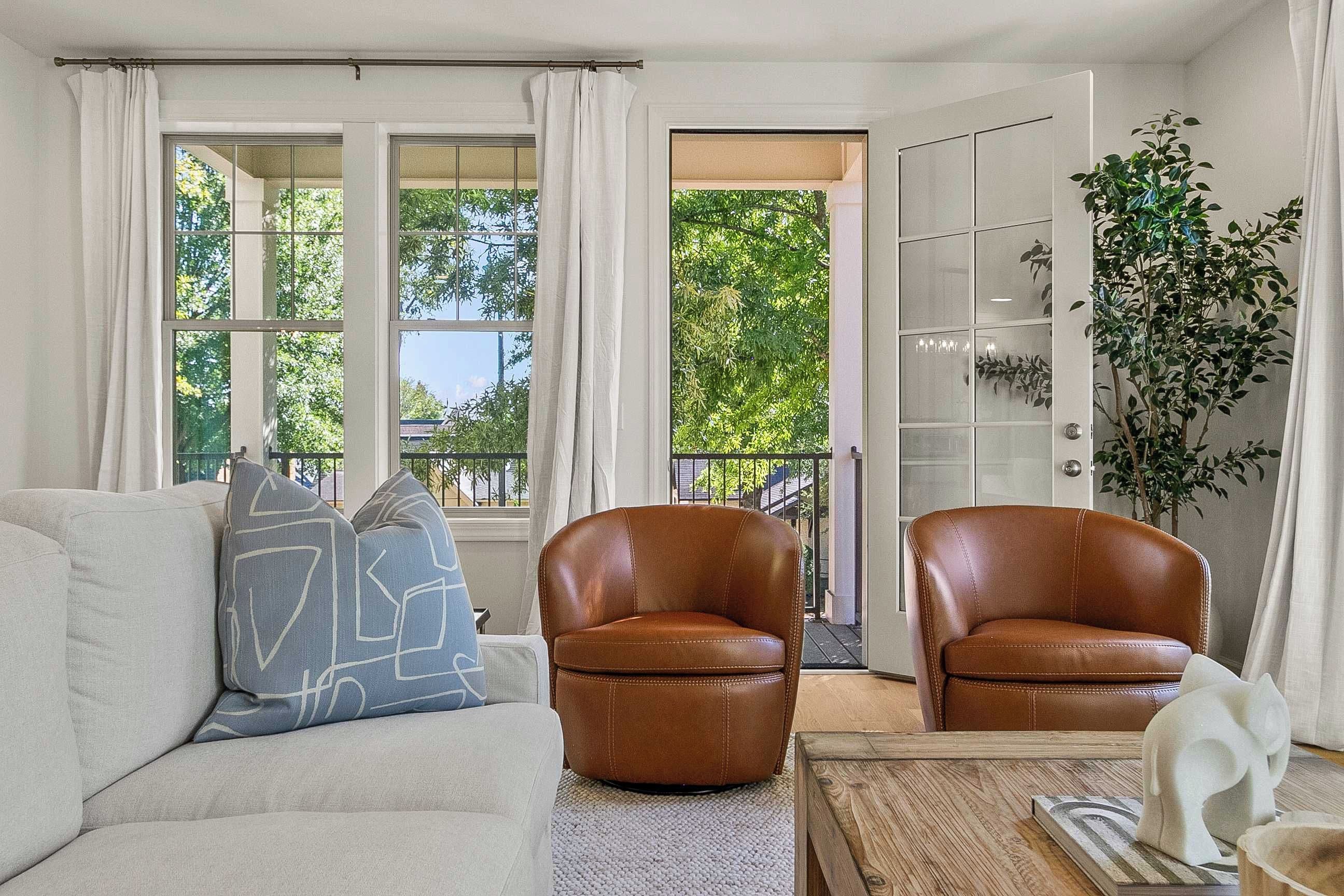 A living room with a sofa, two leather chairs, a coffee table, and a large window with curtains.