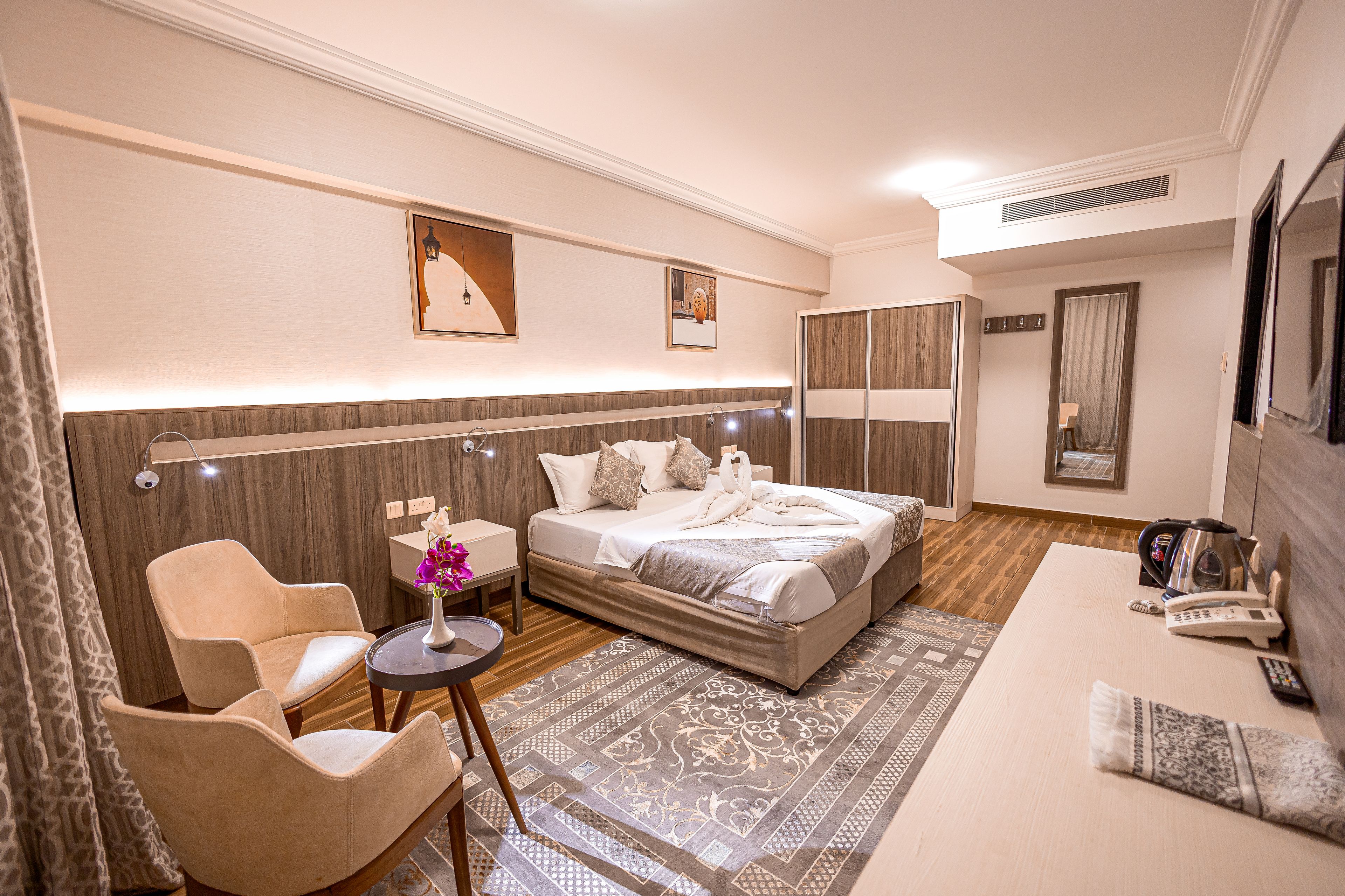A hotel room with a bed, a sofa, a chair, a small table with a vase of flowers, and a telephone.