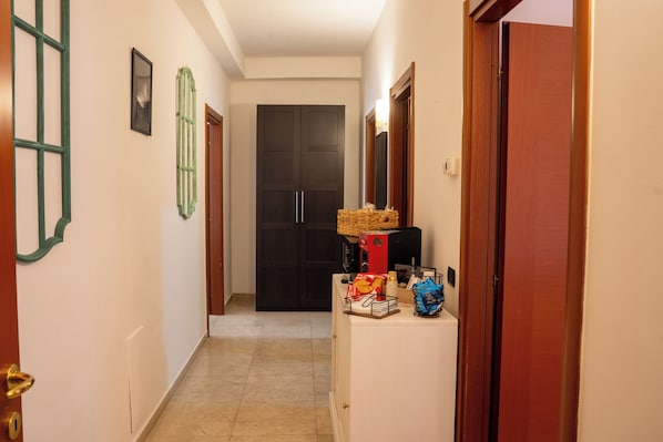 A hallway with a tiled floor, a black door at the end, and a counter with snacks and a basket. - B&B 31mt dal Duomo (Benevento)