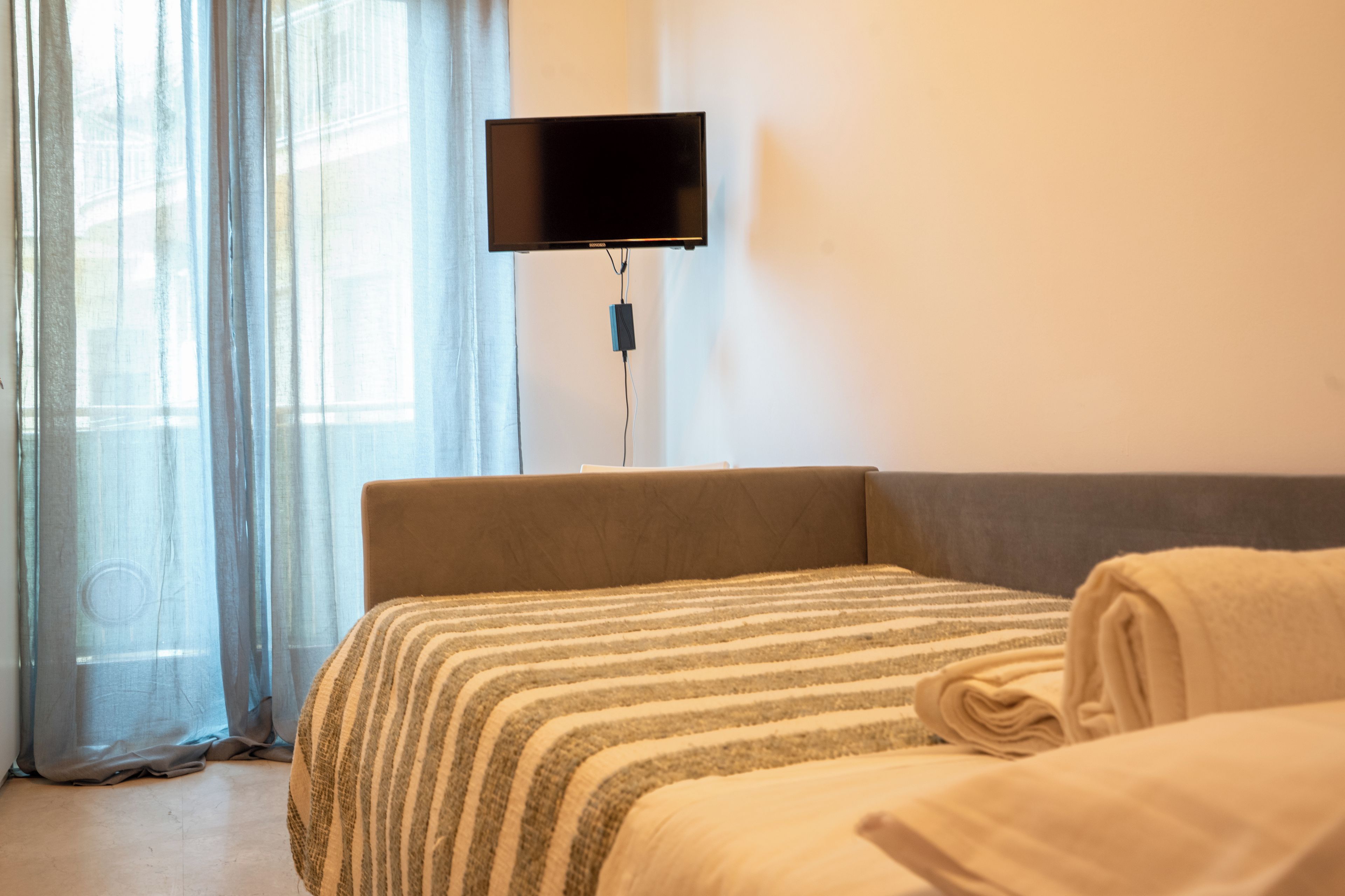 A hotel room with a bed, a TV mounted on the wall, and a window with curtains.