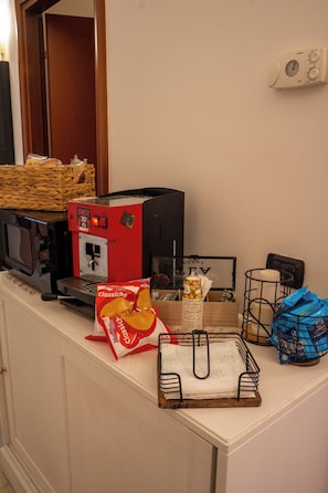 A kitchenette with a coffee machine, a microwave, a basket, a bag of chips, and a coffee cup. - B&B 31mt dal Duomo (Benevento)