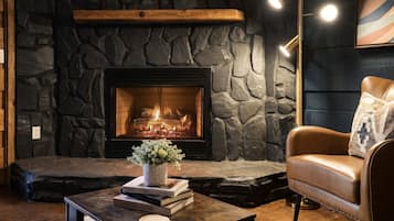 A cozy living room with a stone fireplace, leather armchair, and a coffee table with books and a vase.