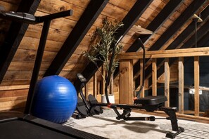 Un gimnasio con equipo de ejercicio, una pelota azul para hacer ejercicio y una planta en maceta en un espacio de ático con piso de madera.