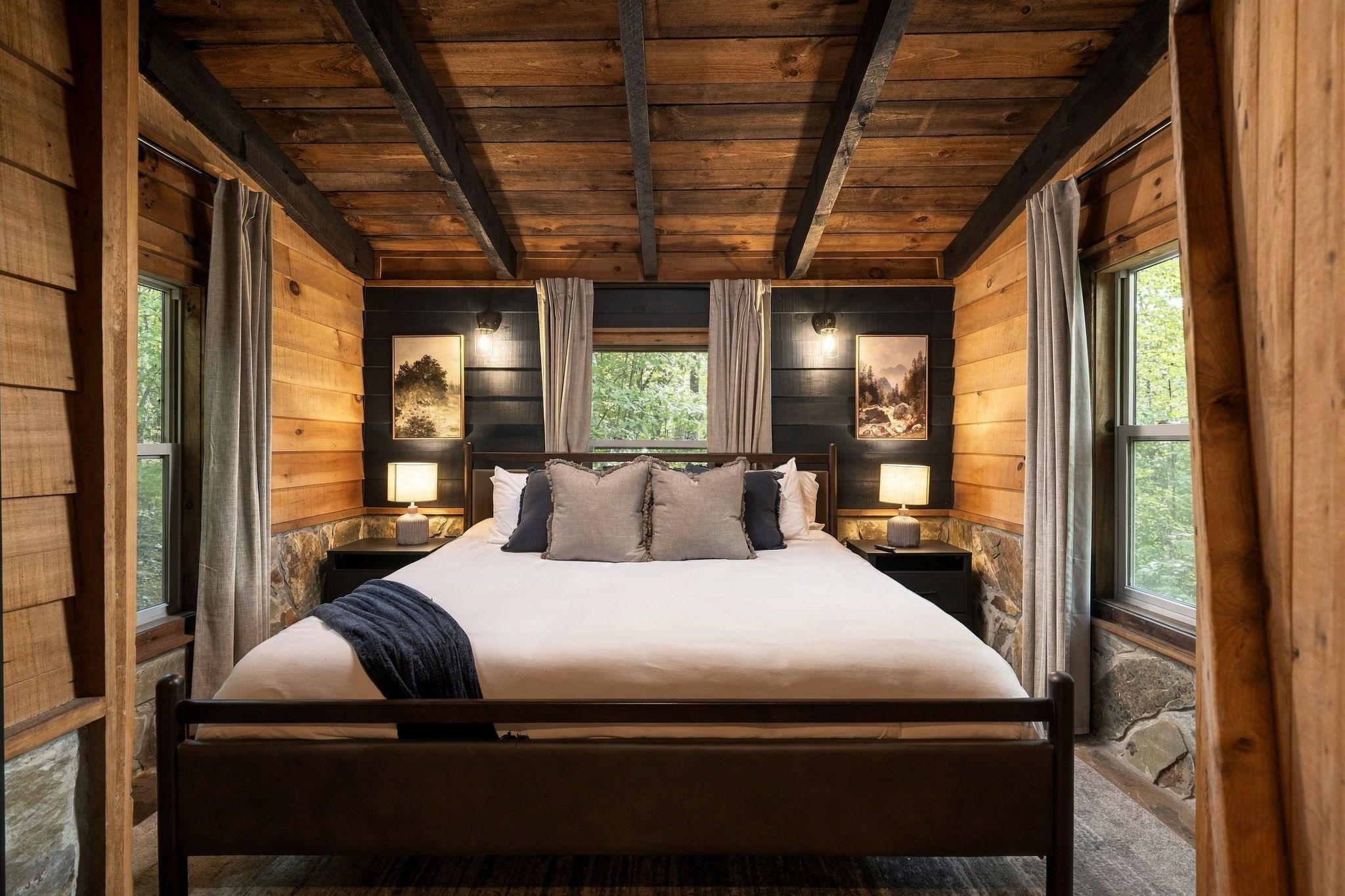 Un dormitorio tipo cabaña de madera con una cama, dos mesitas de noche y dos lámparas.