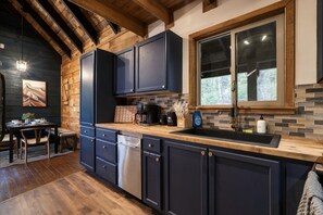 A modern kitchen with dark cabinetry, a wooden countertop, and a large window.