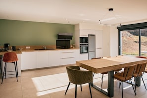Una cocina moderna con comedor, que cuenta con una amplia mesa de madera y sillas, horno empotrado y vista por un gran ventanal.
