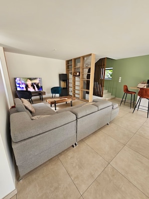 Una sala moderna con un sofá seccional gris, un mueble de entretenimiento de madera y un comedor con mesa y sillas de madera.