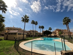 Una piscina envoltada per una tanca, amb palmeres i edificis al fons.