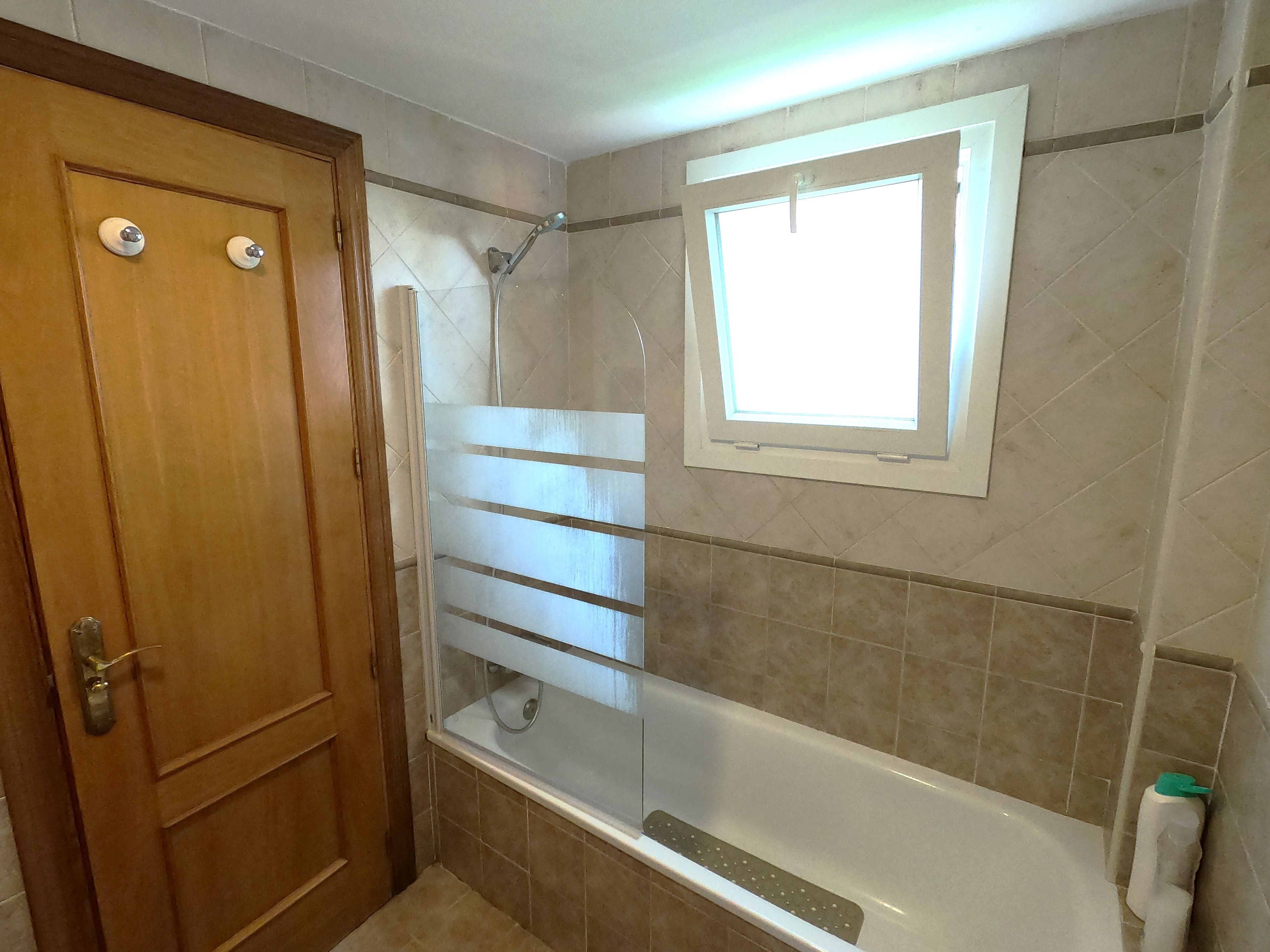 Ein Badezimmer mit Dusche, Badewanne, Fenster und Tür.