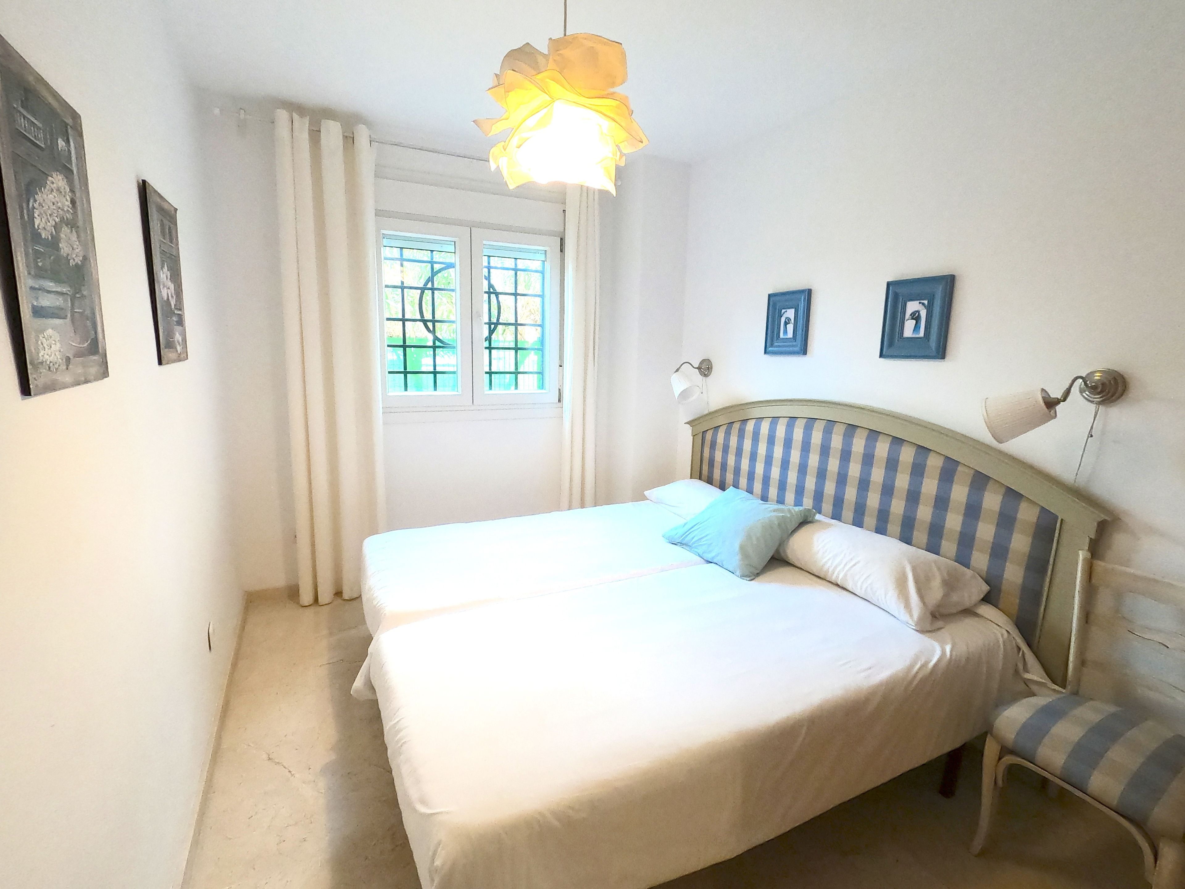 Une chambre avec deux lits, une fenêtre avec des rideaux et une lampe fixée au mur.