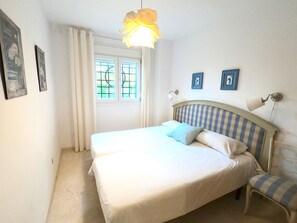 A bedroom with two beds, a window with curtains, and a wall-mounted lamp. - Apartment 'Sunny Terrace by the Golf Course' with Private Terrace, Wi-Fi and Air Conditioning (Vélez-Málaga)