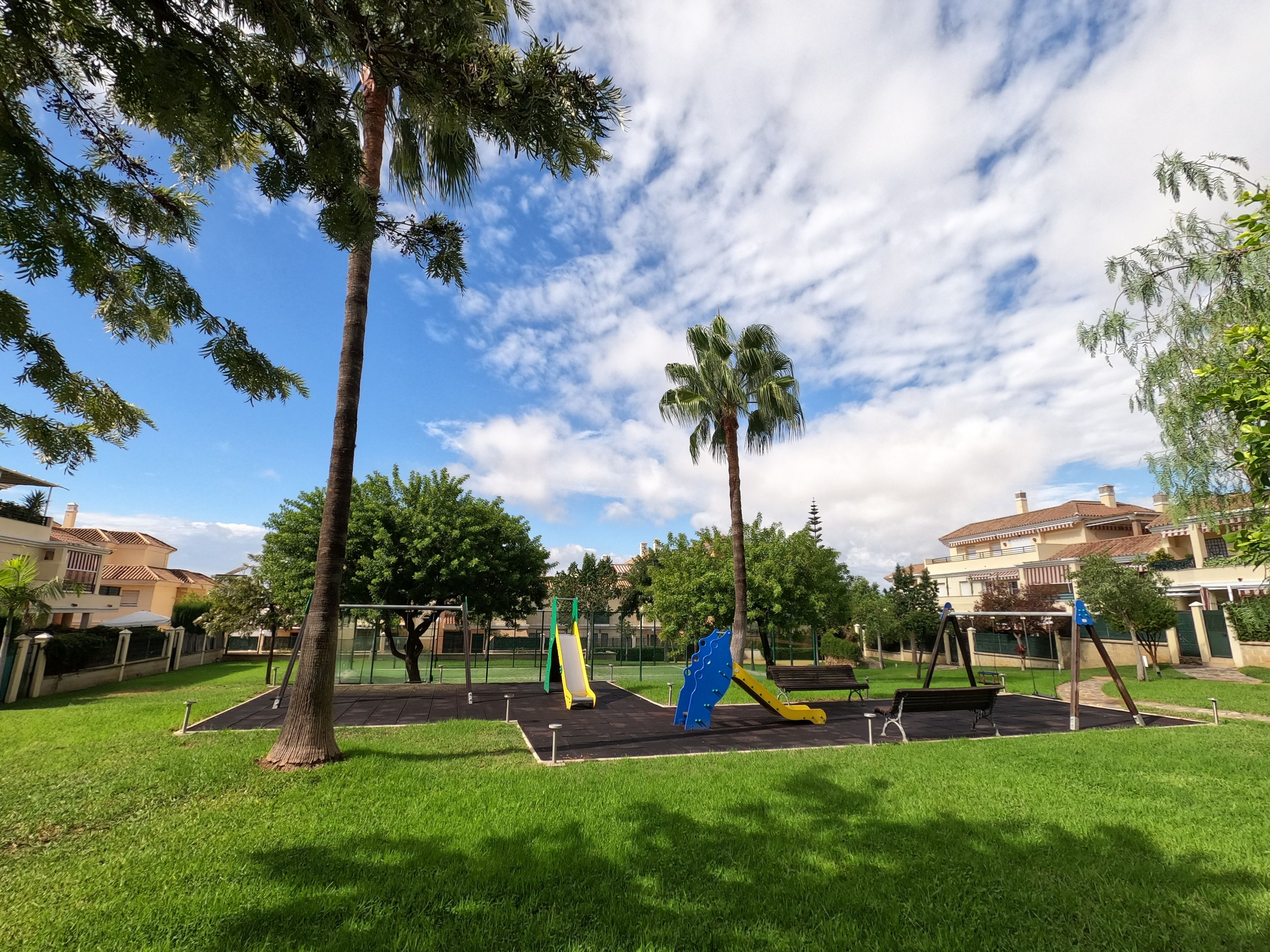 Un parc doté d’aires de jeux pour enfants, comprenant des toboggans et des balançoires, entouré de pelouse et d’arbres.