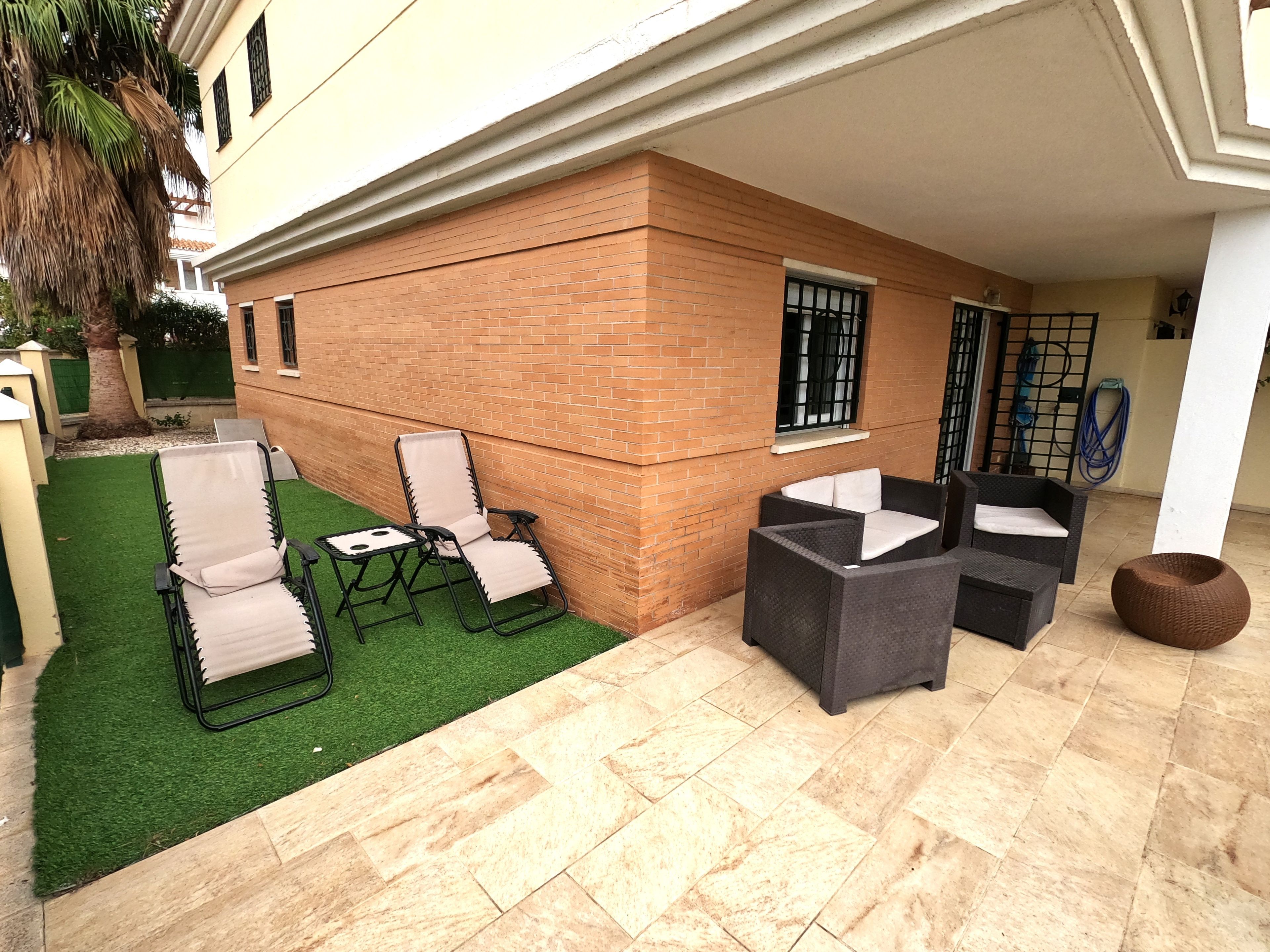 Une terrasse avec des meubles d’extérieur, un mur en briques et une pelouse artificielle verte.