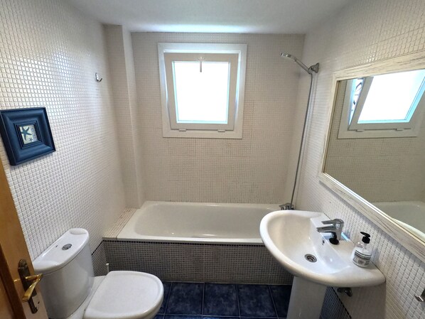 A bathroom with a bathtub, two sinks, a toilet, and a window. - Apartment 'Sunny Terrace by the Golf Course' with Private Terrace, Wi-Fi and Air Conditioning (Vélez-Málaga)