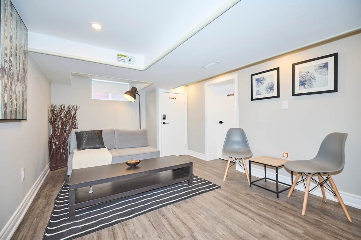 A modern living room with a sofa, coffee table, and chairs, a staircase, and a door with a sign.