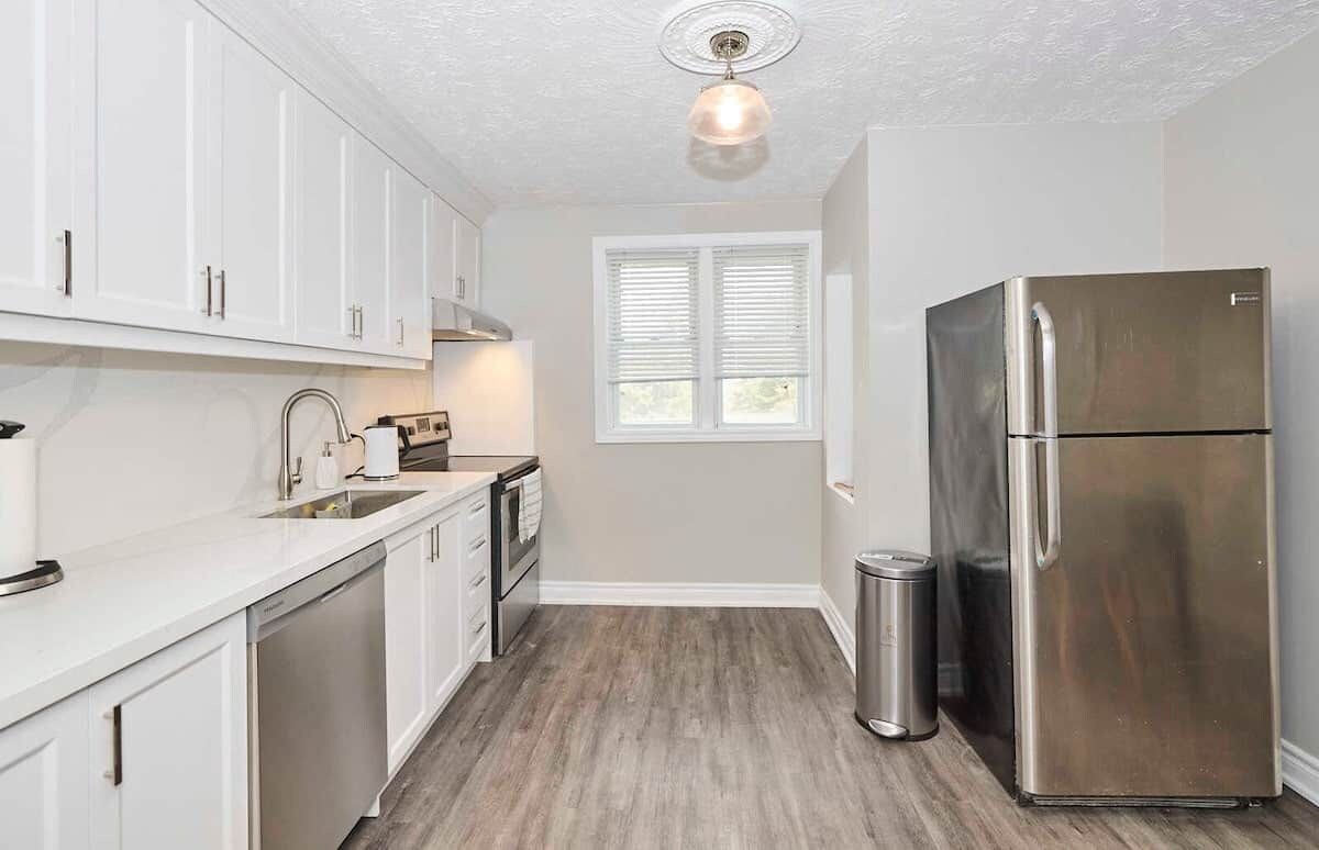 A modern kitchen with white cabinets, stainless steel appliances, and a wooden floor.