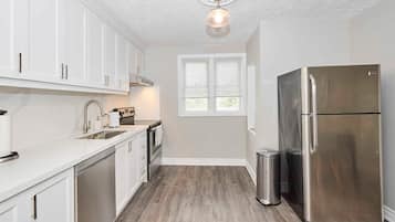 A modern kitchen with white cabinets, stainless steel appliances, and a wooden floor.