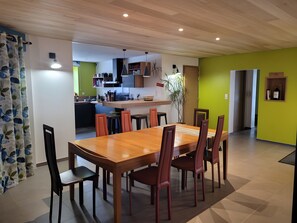 Ein Essbereich mit Holztisch und -stühlen, im Hintergrund eine Küche und eine Wand in Grüntönen.