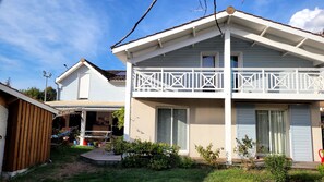 Ein zweistöckiges Haus mit Balkon, Holzterrasse und kleinem Garten.