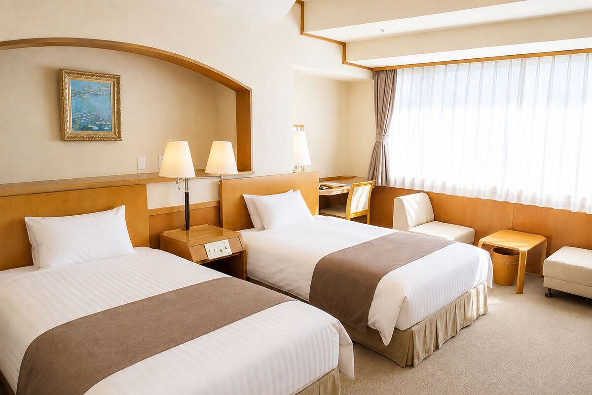 A hotel room with two beds, a desk, a chair, and a window with curtains.