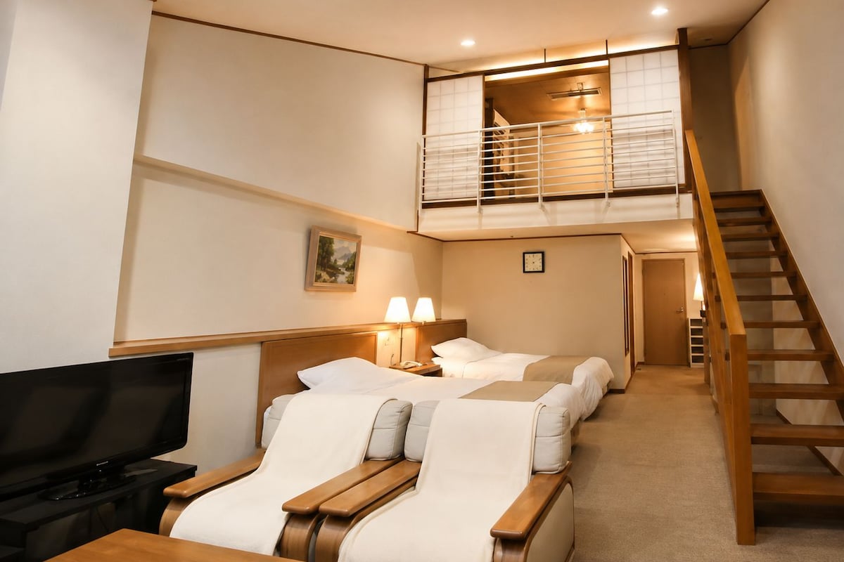 A hotel room with a TV, two beds, a balcony, and a staircase.