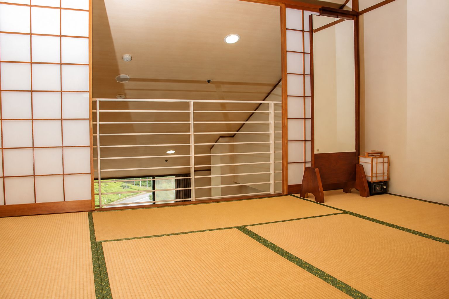A traditional Japanese room with tatami flooring, shoji screens, and a view of a green landscape.