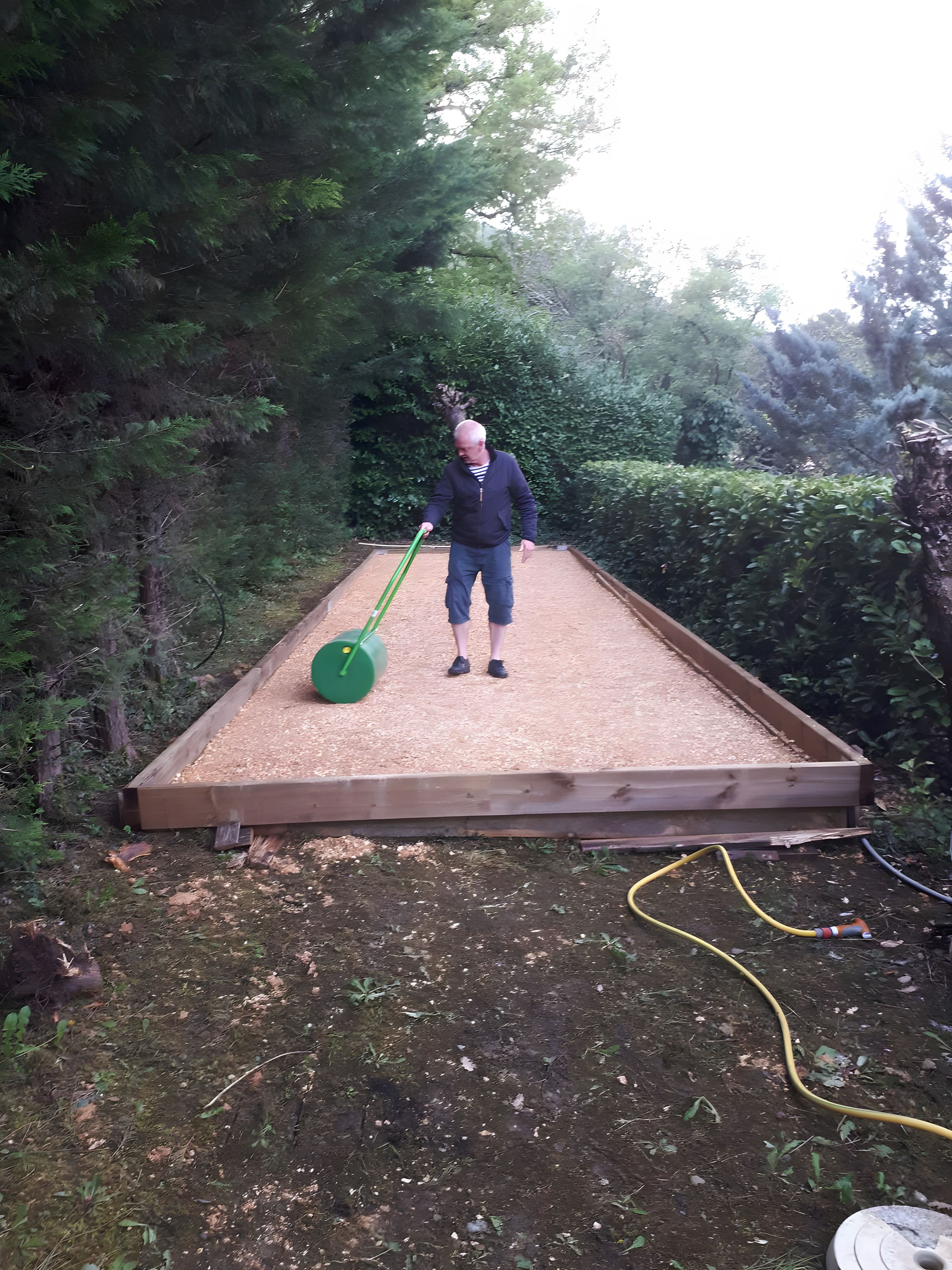 Eine Person steht auf einer Holzdielen-Terrasse mit einem grünen Rasenmäher.