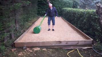 Eine Person steht auf einer Holzdielen-Terrasse mit einem grünen Rasenmäher.