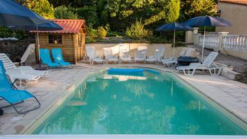 Ein Swimmingpool mit Liegestühlen und Sonnenschirmen, umgeben von Bäumen und einem kleinen Gebäude.