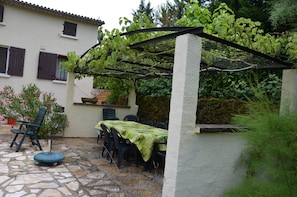 Un patio con mesa y sillas, una pérgola con plantas trepadoras y suelo de piedra.