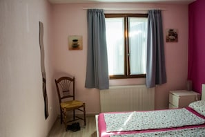Un dormitorio con una cama, una silla, un radiador y una ventana con cortinas.