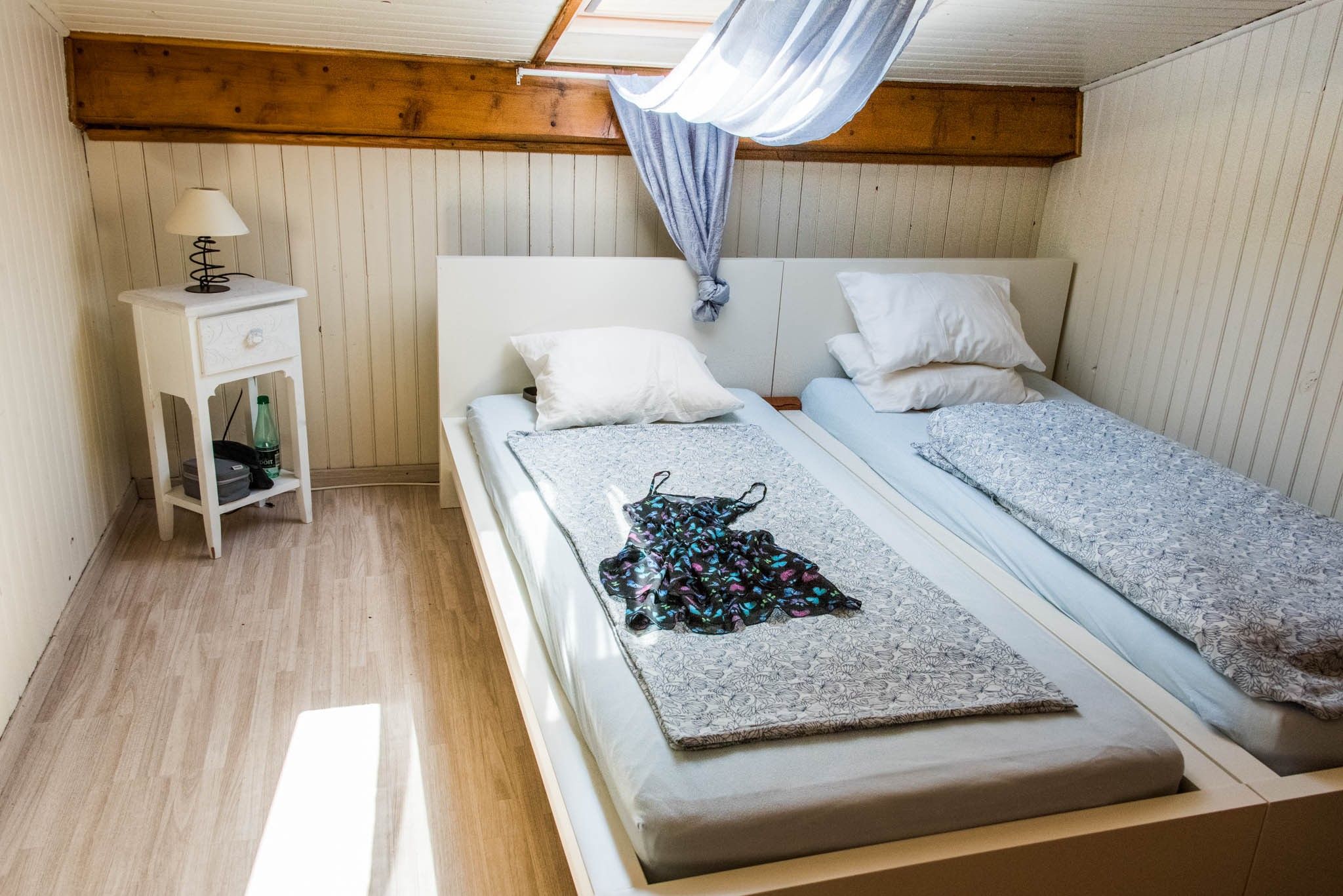 Ein Schlafzimmer mit Holzboden, einem Bett mit gemustertem Bettbezug, einem Nachttisch mit Lampe und einem Kleiderschrank.
