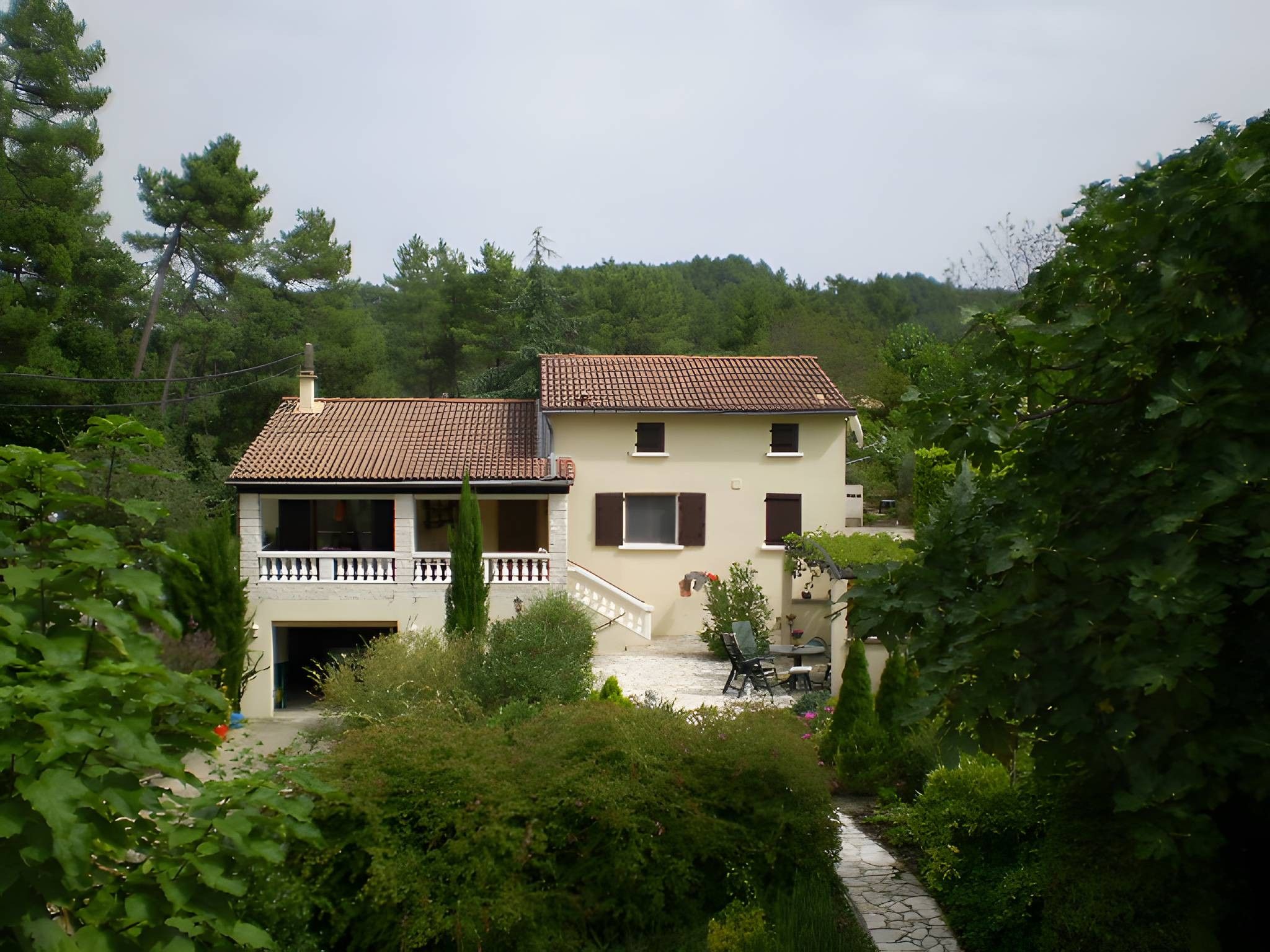 Ein zweistöckiges Haus mit Ziegeldach, einem Balkon und einem Garten mit einem Weg.