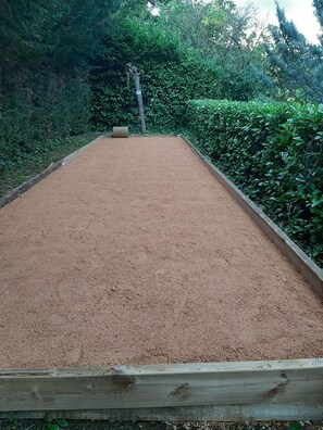 A rectangular outdoor area with a sandy surface, surrounded by dense greenery.