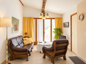 A living room with a sofa, armchairs, a table, a lamp, a plant, and a clock on the wall.