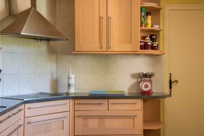 Una cocina con armarios de madera, una campana extractora de acero inoxidable, una balanza y un especiero.