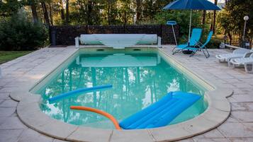 Ein Swimmingpool mit einer umlaufenden Sonnenterrasse, Liegestühlen und einer Sitzbank.
