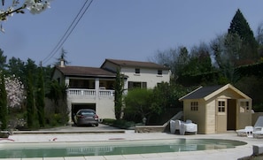 Una casa de dos pisos con piscina, un auto estacionado adelante y un cobertizo pequeño.