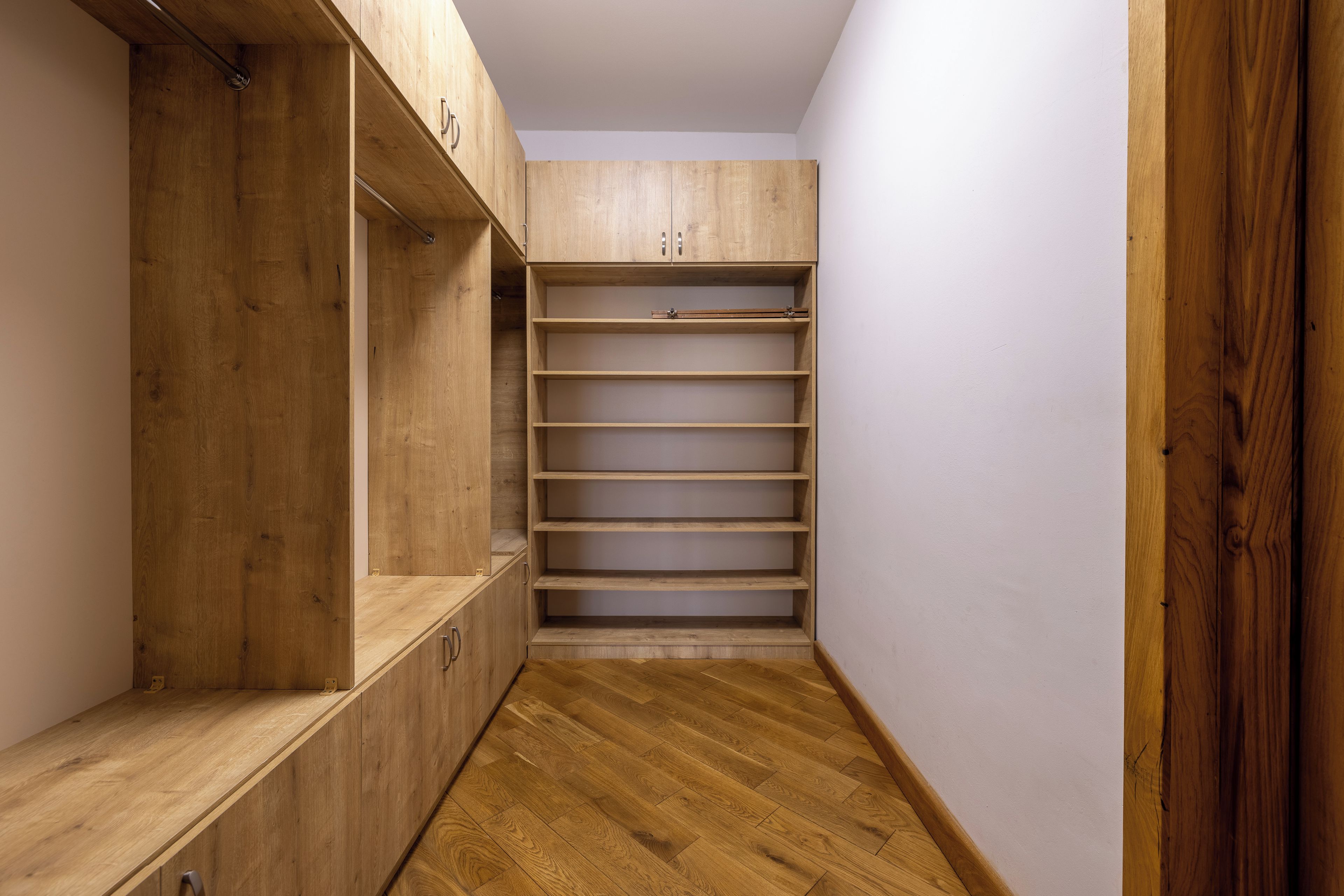 A narrow hallway with wooden flooring leading to a closet with open shelving and a built-in bench.