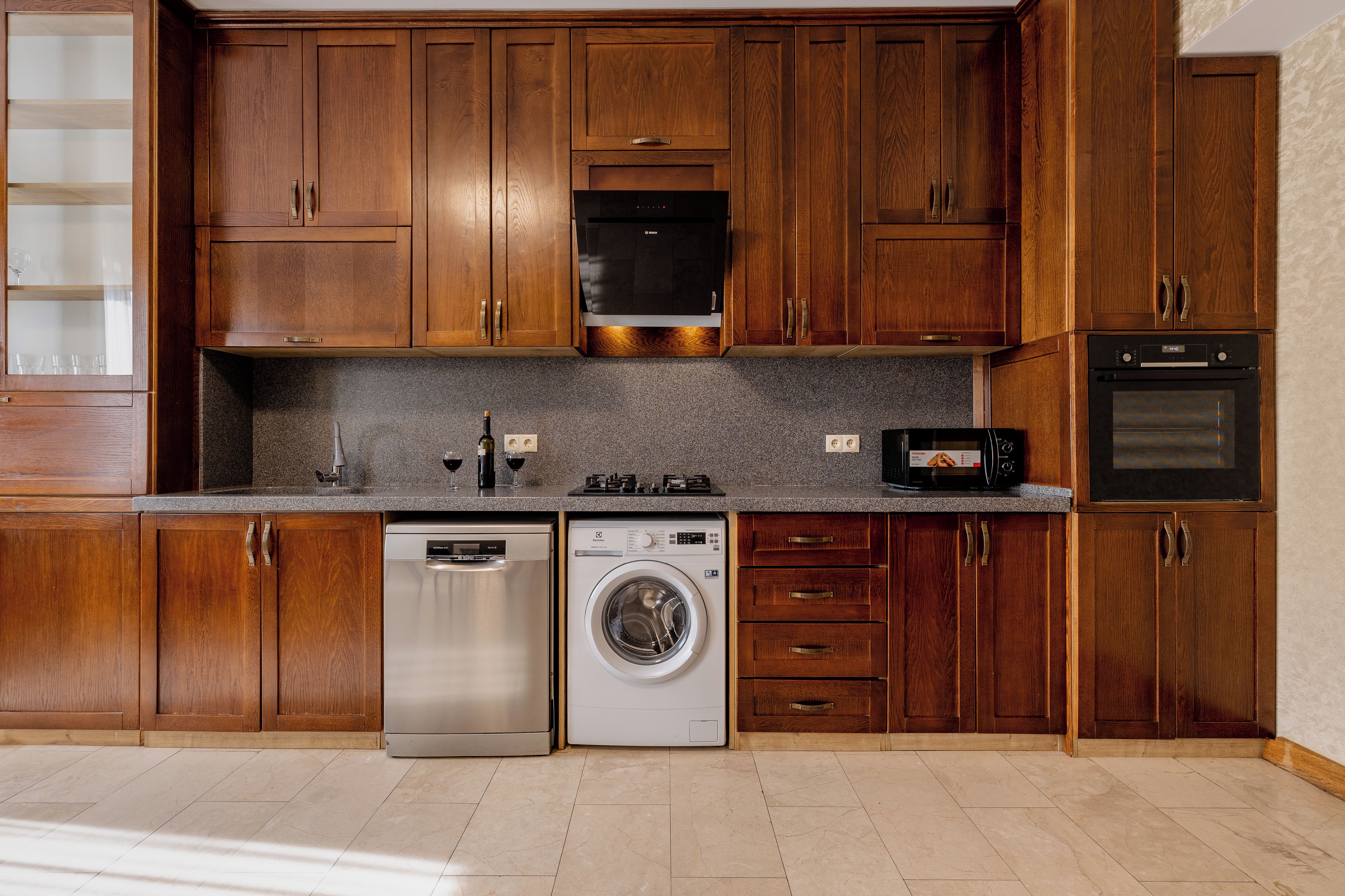 A kitchen with wooden cabinets, a dishwasher, a washing machine, a microwave, and an oven.