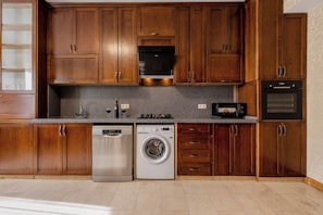 A kitchen with wooden cabinets, a dishwasher, a washing machine, a microwave, and an oven. - Marvelous 5-bedroom apartment with AC in charming Tbilisi (Tbilisi)