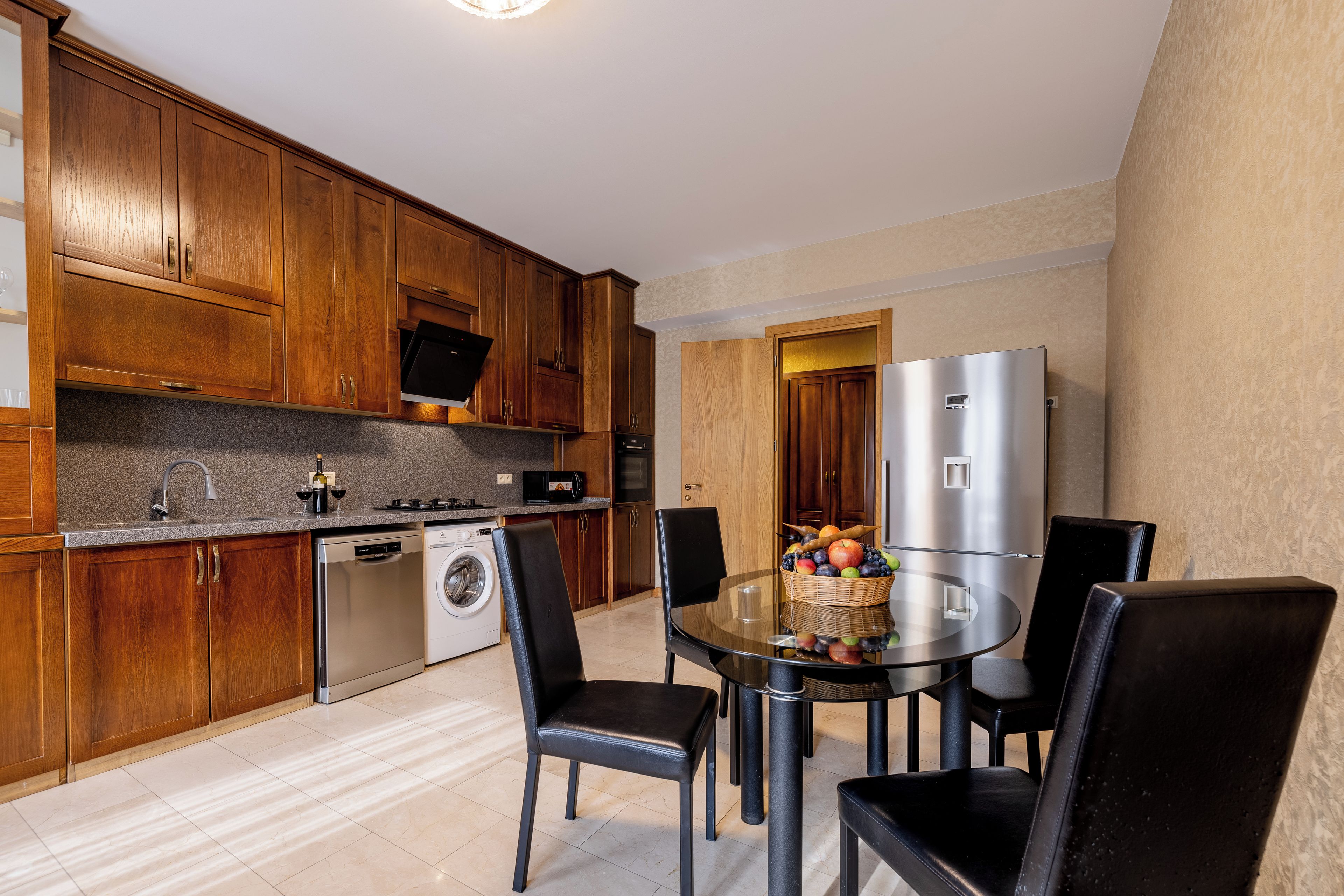A modern kitchen with wooden cabinets, a stainless steel refrigerator, a dishwasher, and a dining table with chairs.