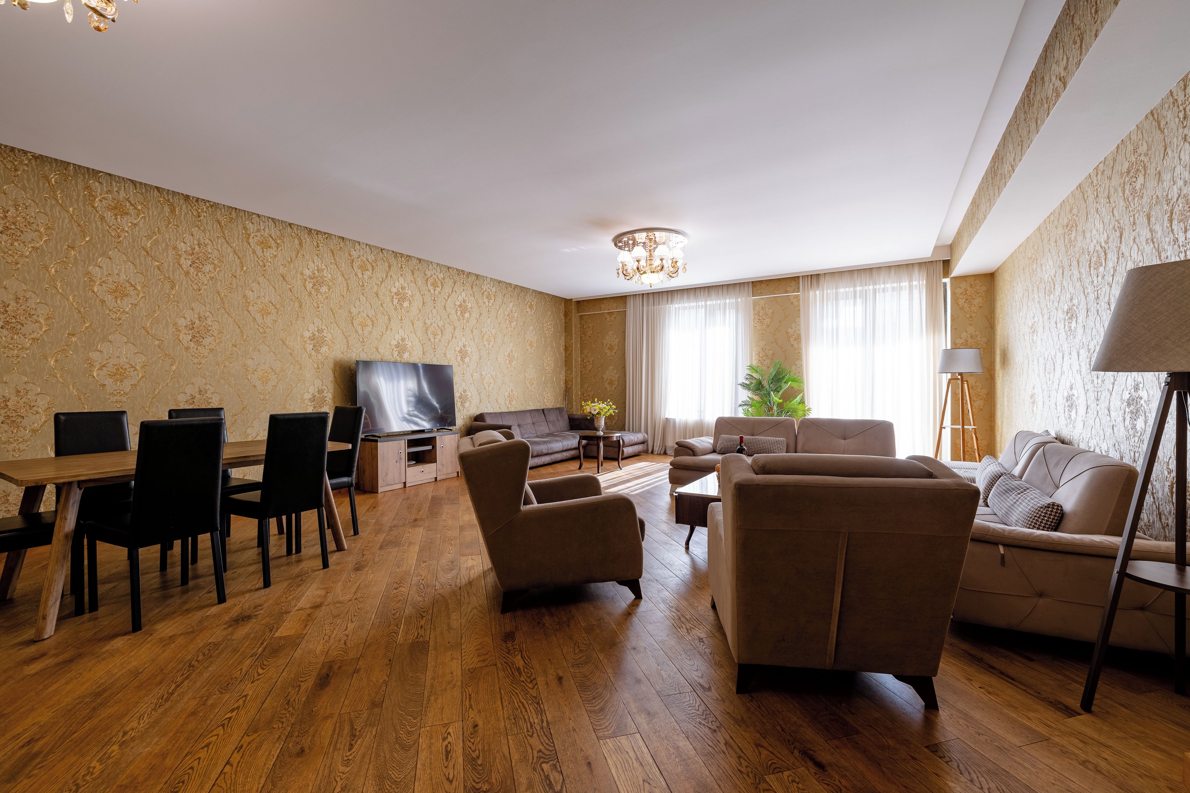 A living room with a wooden floor, a sofa set, a dining table with chairs, a TV, and a chandelier.