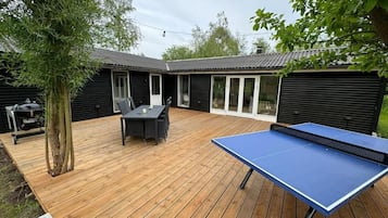 Um deck externo com mesa de pingue-pongue, mesa de jantar e cadeiras.