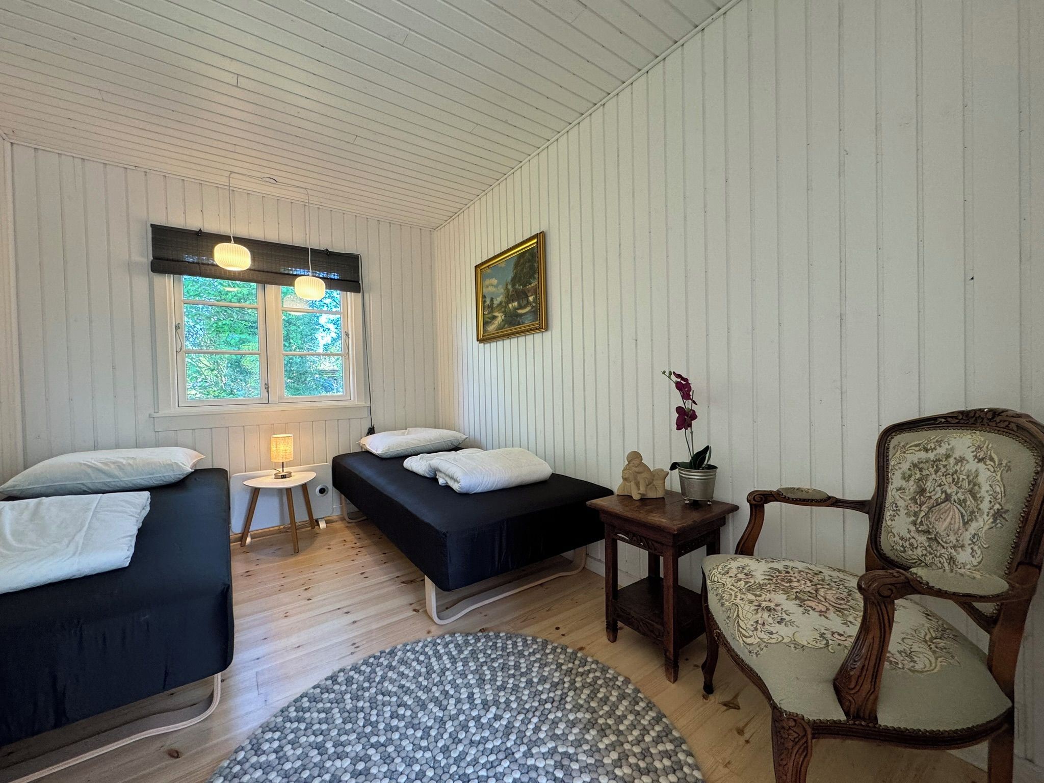 Ein Zimmer mit zwei Betten, einem Sessel, einem kleinen Tisch und einem Bild an der Wand.