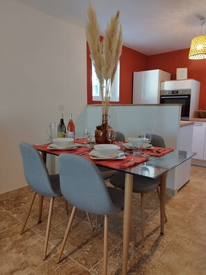 Un coin repas avec une table en verre, des chaises bleues et un vase contenant des plumes d’herbe de la pampa.