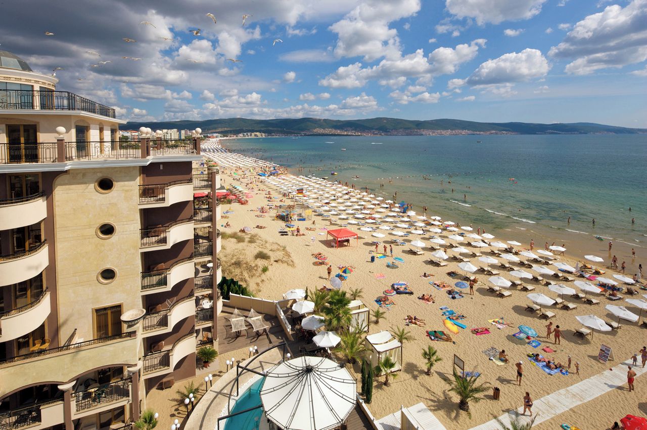 Un hotel con varios balcones con vistas a una playa con sombrillas y sillas de descanso.